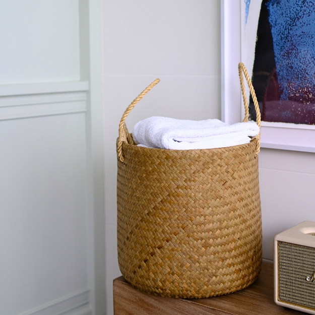 Tung Pha basket placed on a wooden side cabinet in a white minimalist room, filled with neatly folded white towels.
