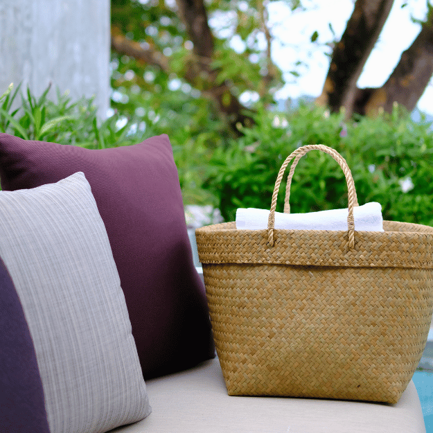 Tung Yai basket on an outdoor daybed, surrounded by plush cushions, holding fresh white towels against a natural backdrop.