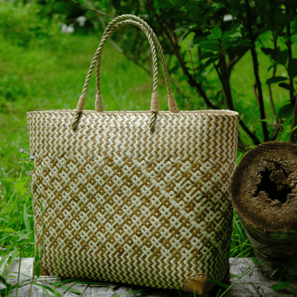 Handwoven Chanita tote in white and gold geometric weave resting against a textured tree stump in lush greenery.