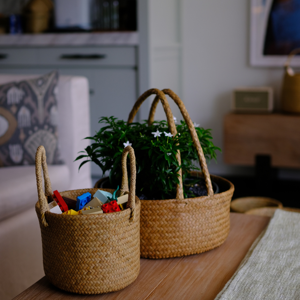 Two Tung Dek baskets placed in a living space—one filled with children’s toys, the other with greenery—demonstrating their dual use for storage or decorative accents.