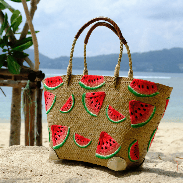 Side angle of the Watermelon Bites tote photographed on a sandy beach with ocean in the background, showing its structured silhouette and fine detailing.