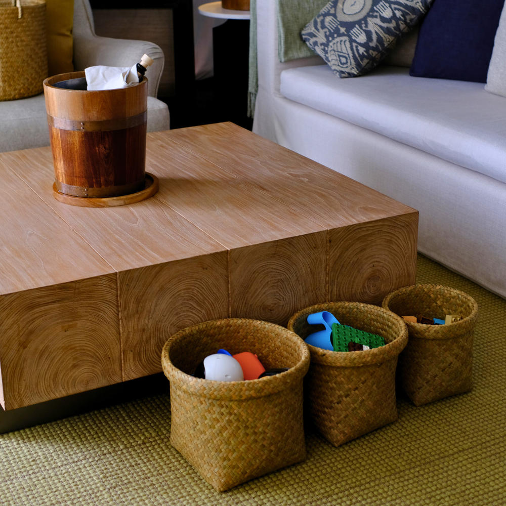 Three Ton Rak baskets in graduated sizes holding assorted items, arranged beside a square wooden coffee table in a modern living room.