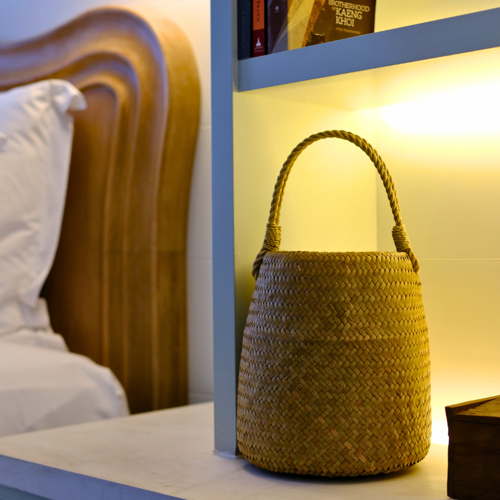 Toong Nom displayed on a glowing shelf beside a carved wood bedframe, moody lighting.