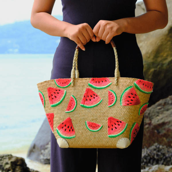 Model holding the Watermelon Bites tote at waist height, highlighting the bag’s full shape and playful watermelon embroidery against a neutral outfit.