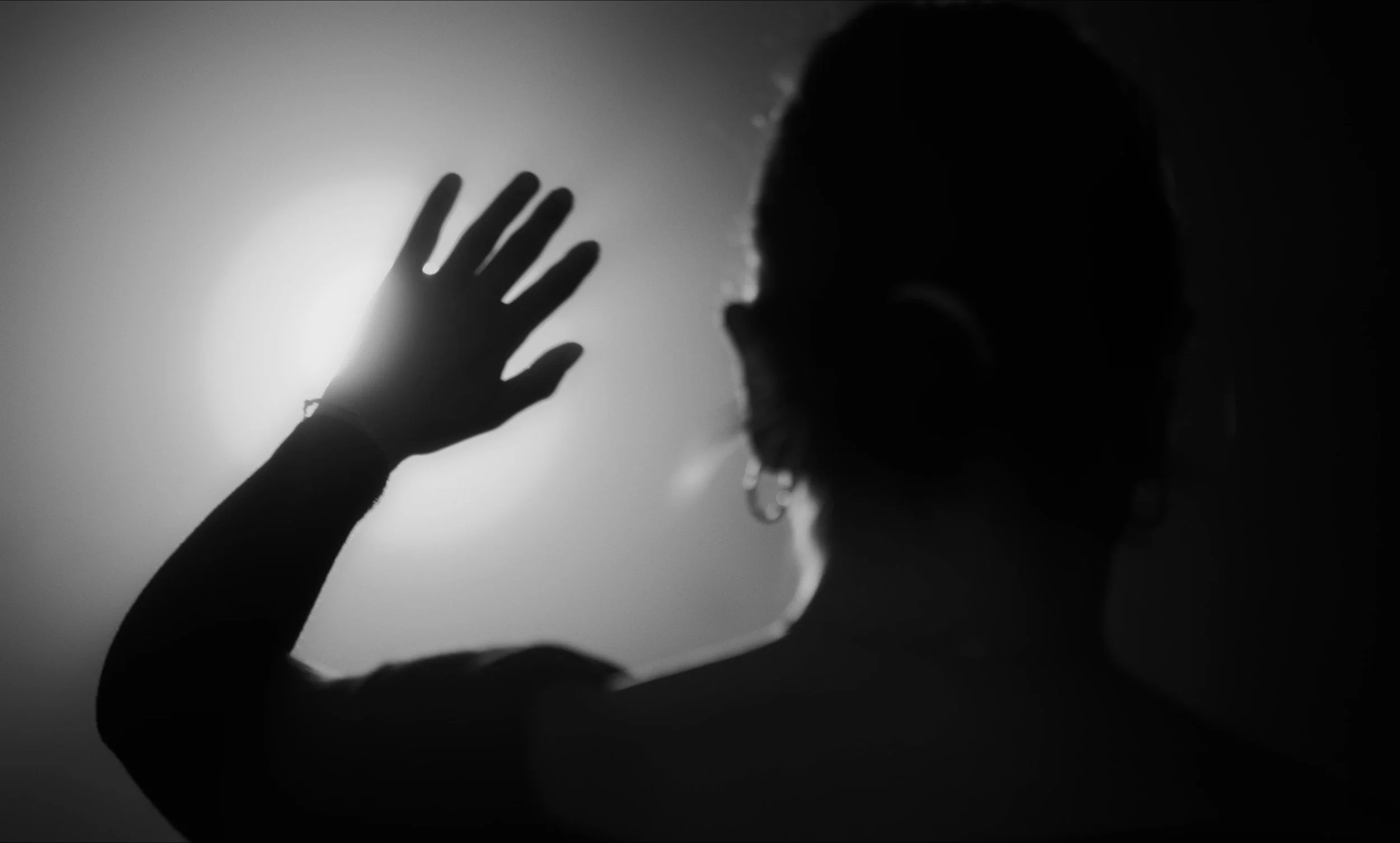 Silueta de una persona levantando la mano hacia una fuente de luz en un fondo en blanco y negro.