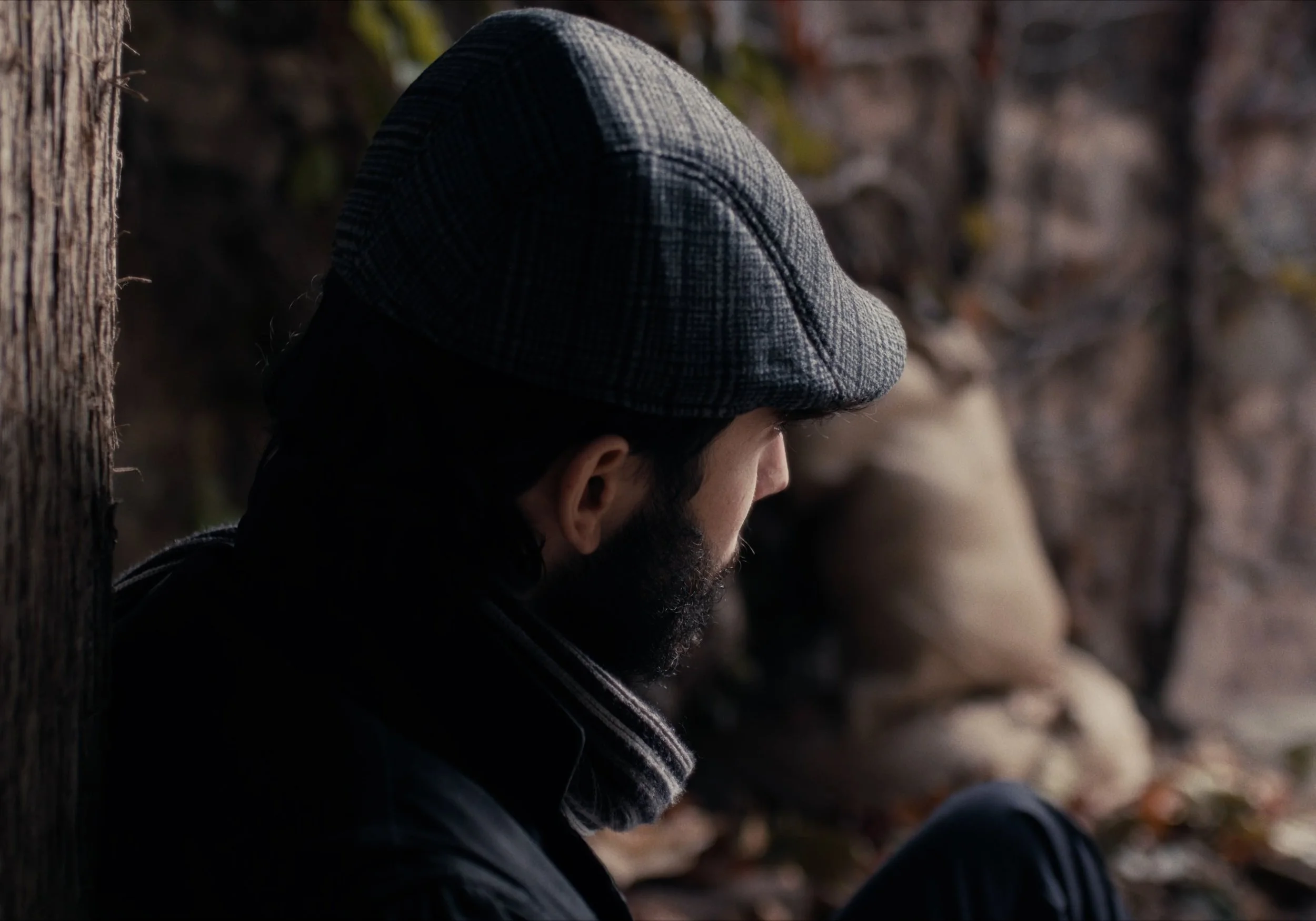 Hombre de perfil con gorra y bufanda en ambiente exterior.