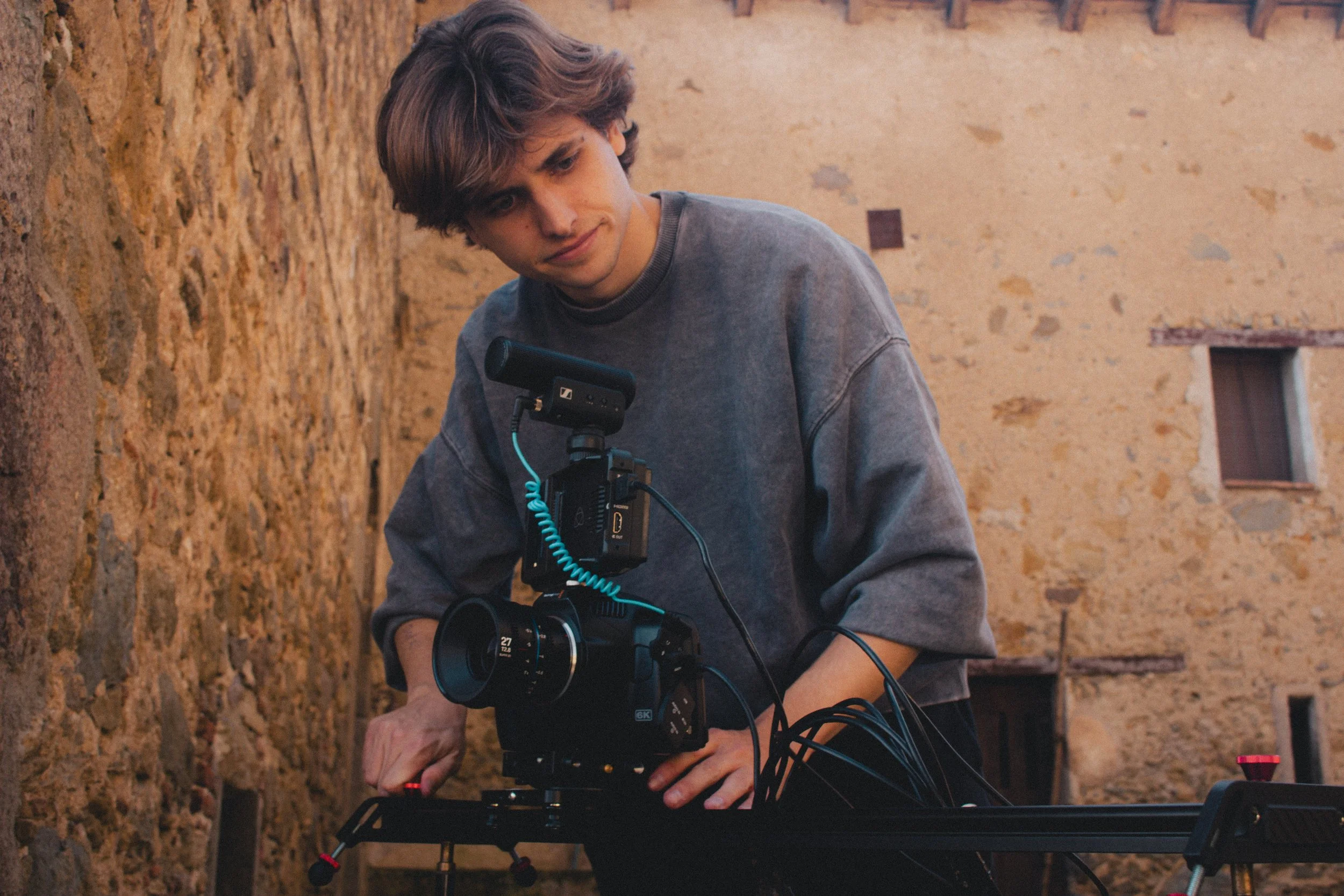 Persona operando una cámara de cine en un entorno al aire libre con paredes de piedra.