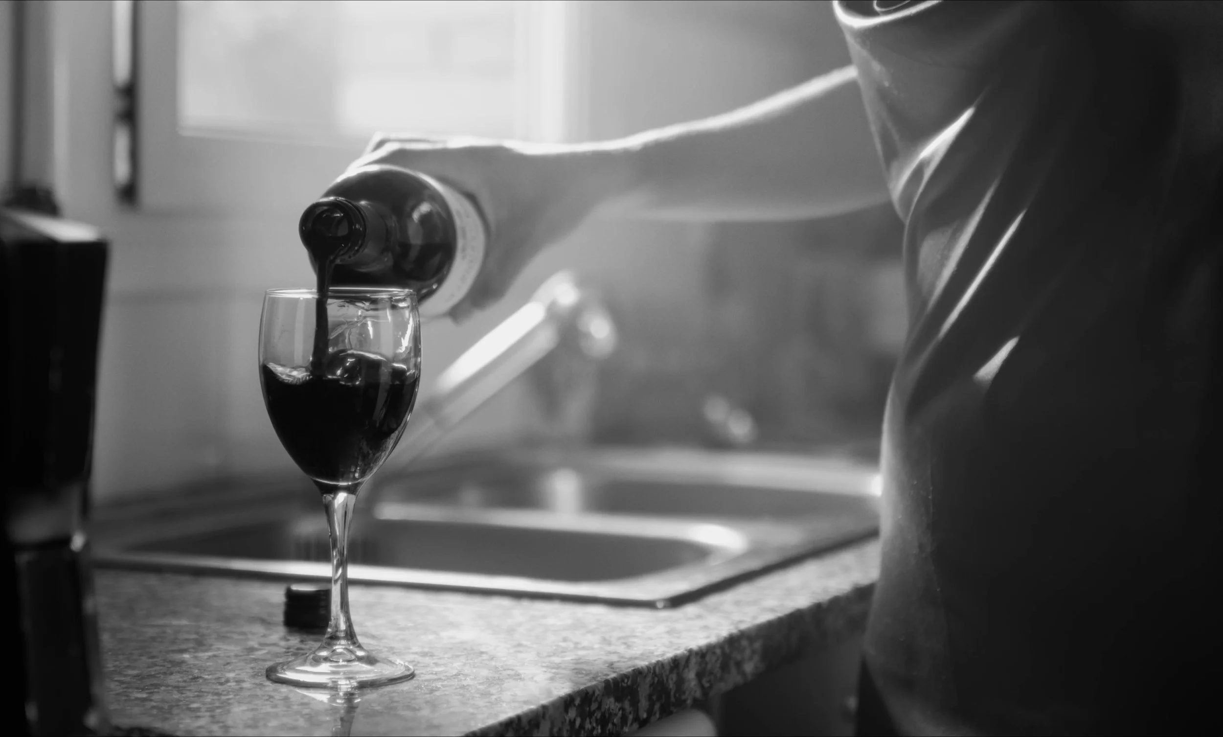 Persona sirviendo vino tinto en una copa sobre una encimera de cocina.