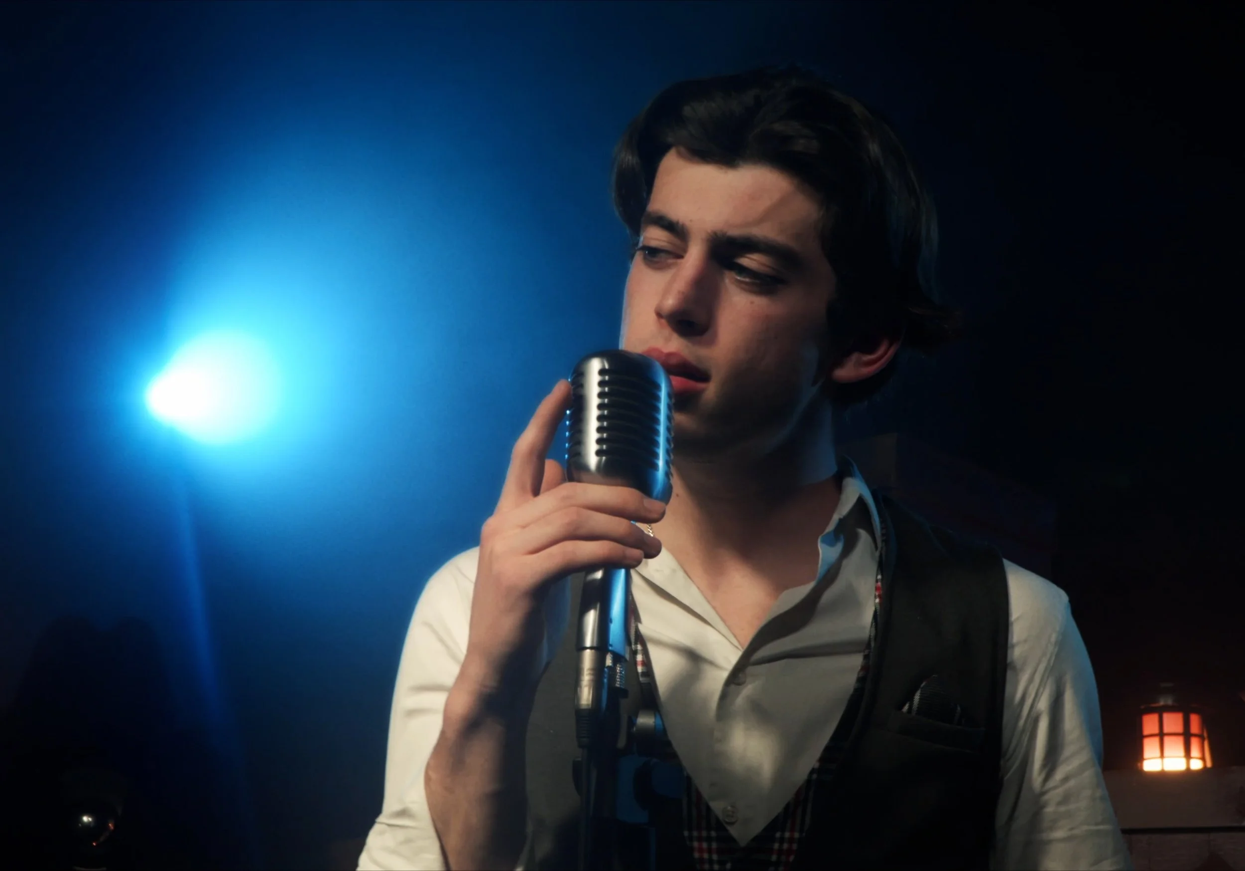 Hombre joven cantando en un micrófono en un ambiente con iluminación azul.