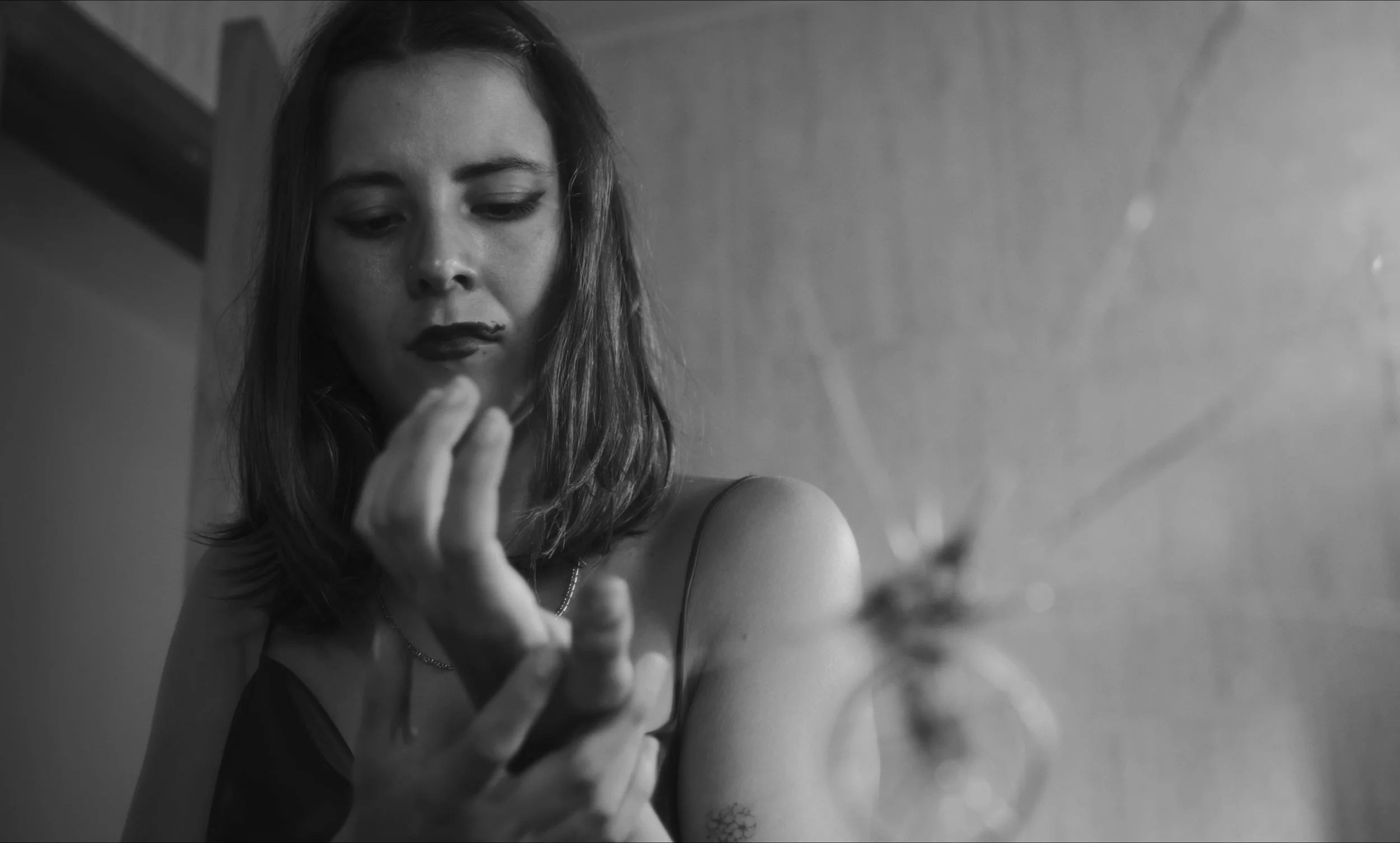 Mujer joven en blanco y negro tocando sus dedos frente a un espejo roto.