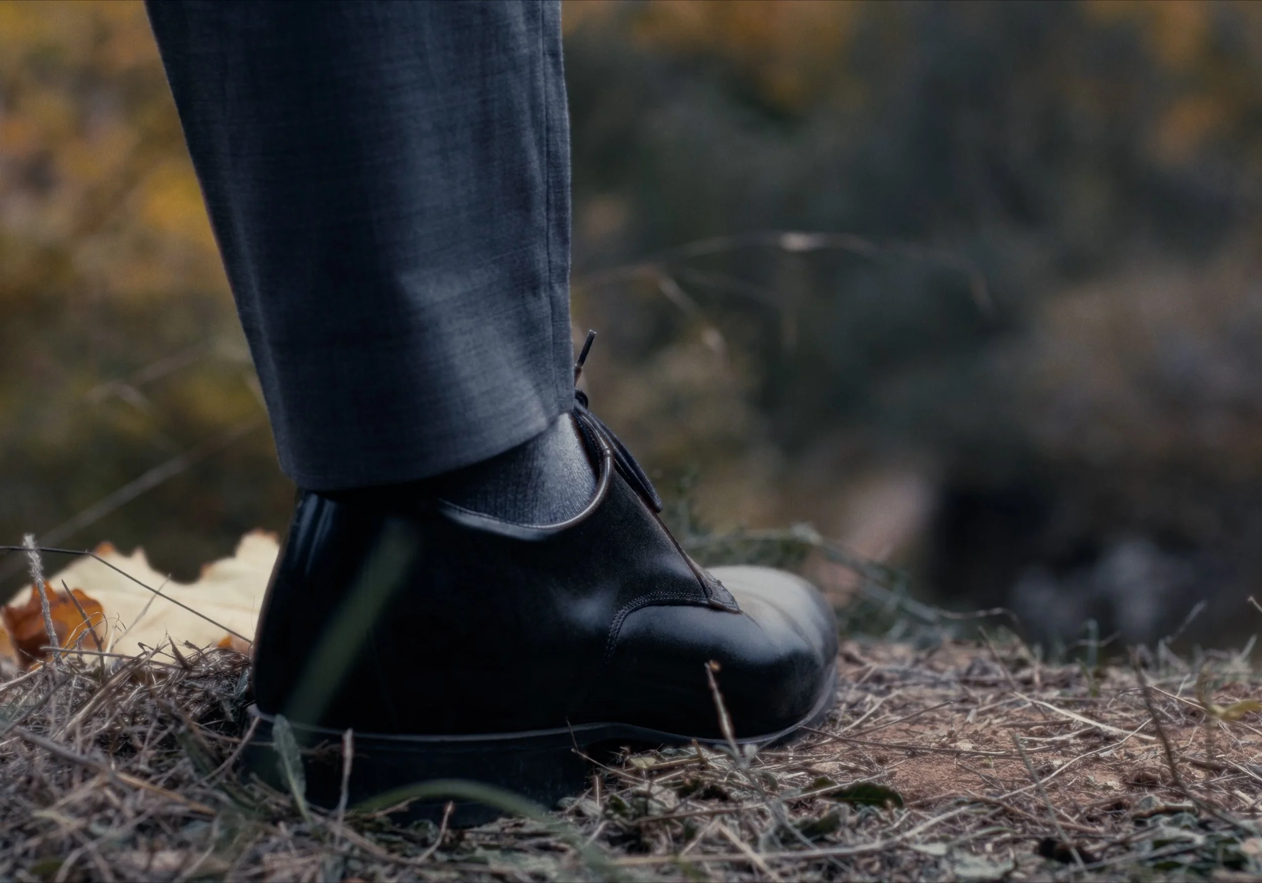 Pie masculino en zapatos formales negros sobre hierba seca, primer plano.