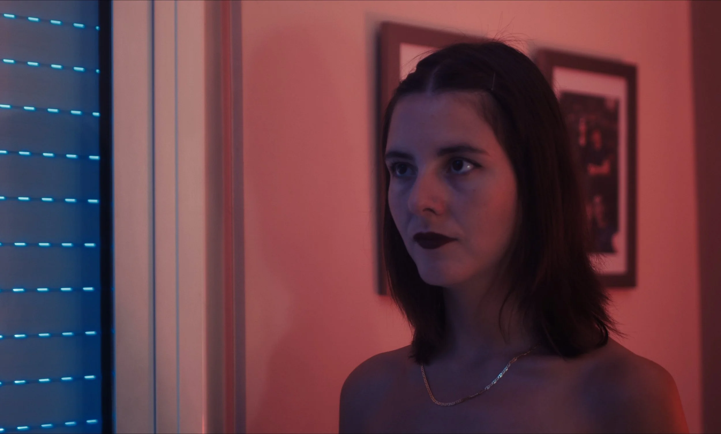 Mujer joven con expresión seria, iluminada por luces azules y rojas.