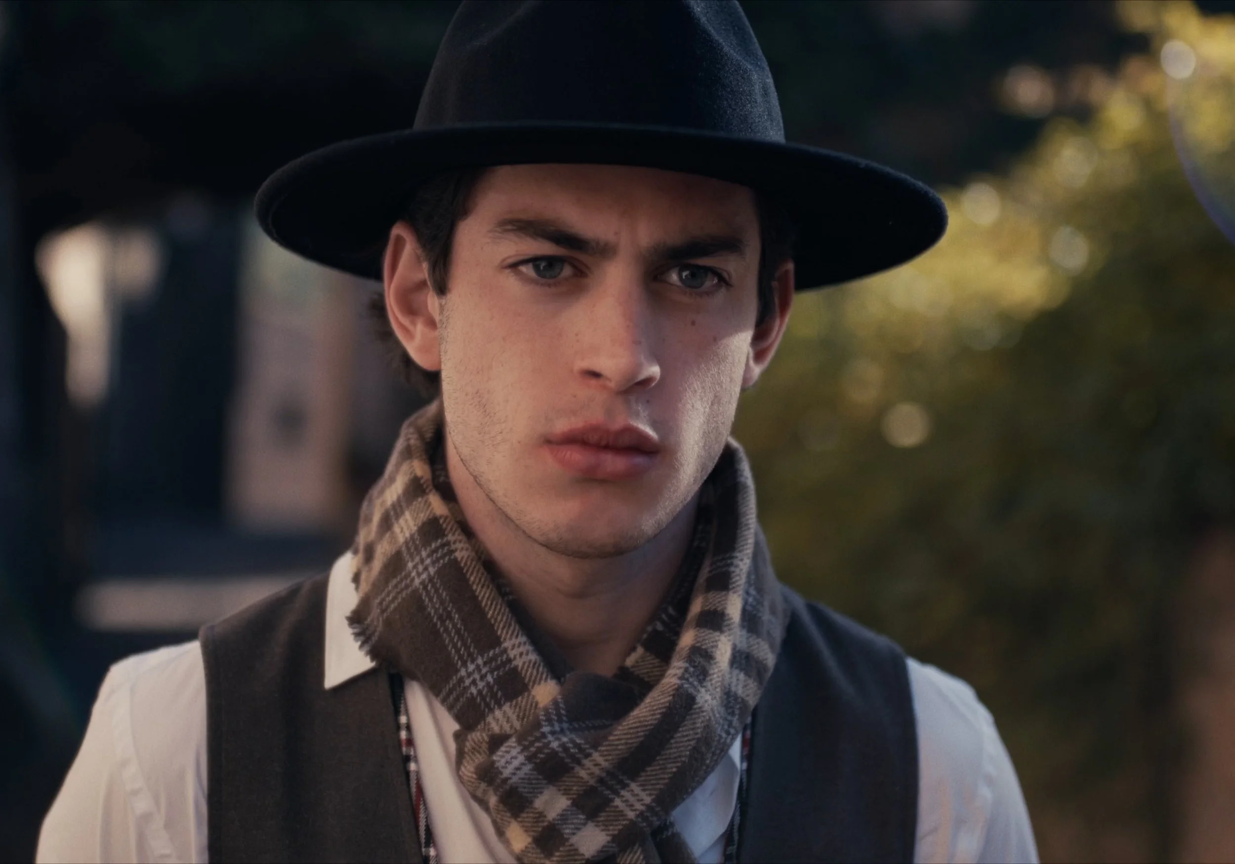 Hombre joven con sombrero y bufanda en un entorno al aire libre.