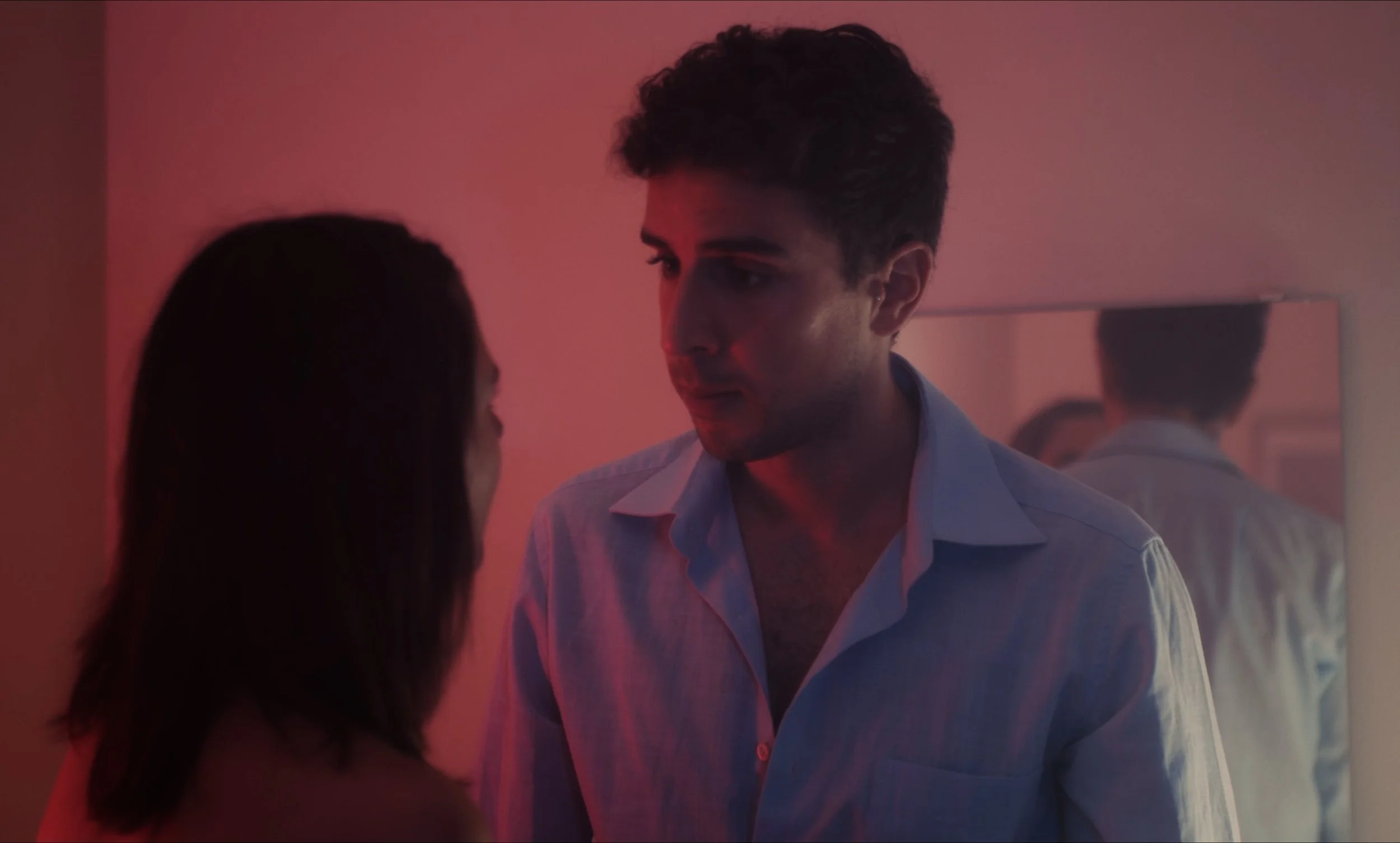 Dos personas mirándose, con luz tenue y un espejo en el fondo.
