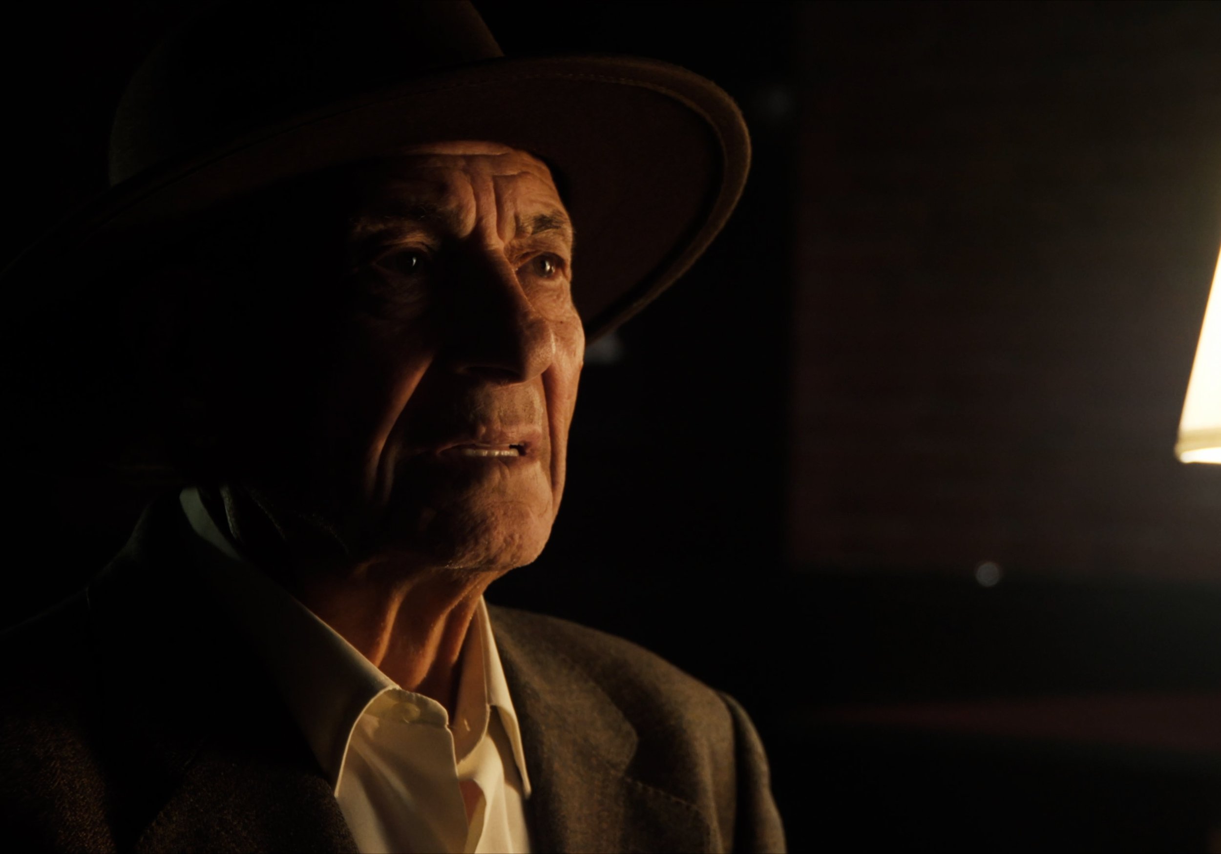 Hombre mayor con sombrero, iluminado dramáticamente de perfil, fondo oscuro.