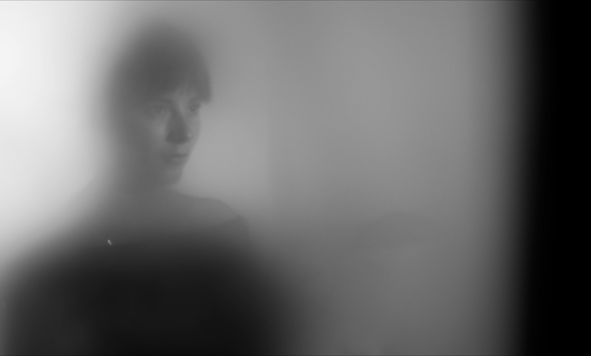 Figura humana borrosa detrás de vidrio empañado en blanco y negro.