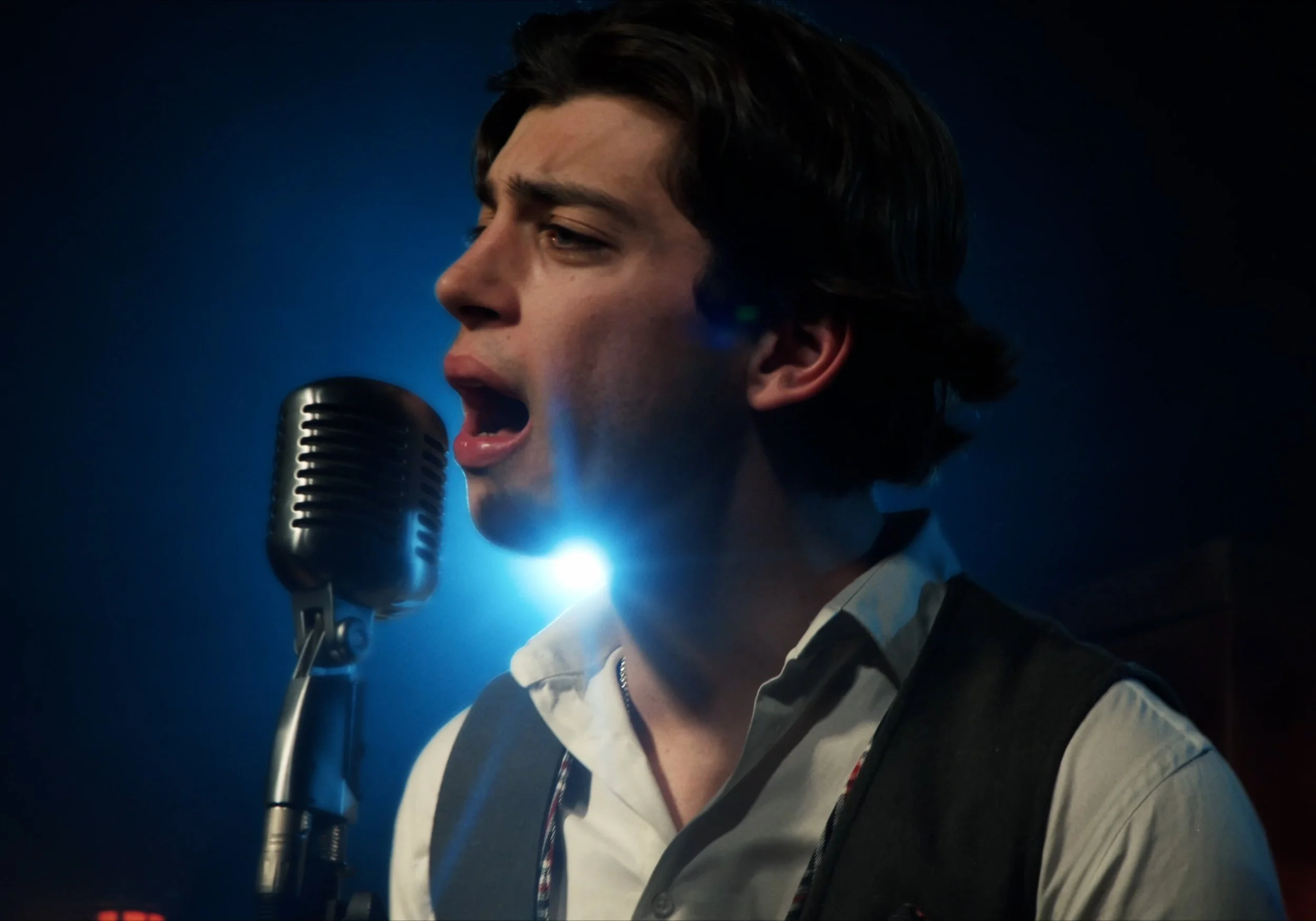 Cantante con micrófono antiguo en escenario con luz azul.