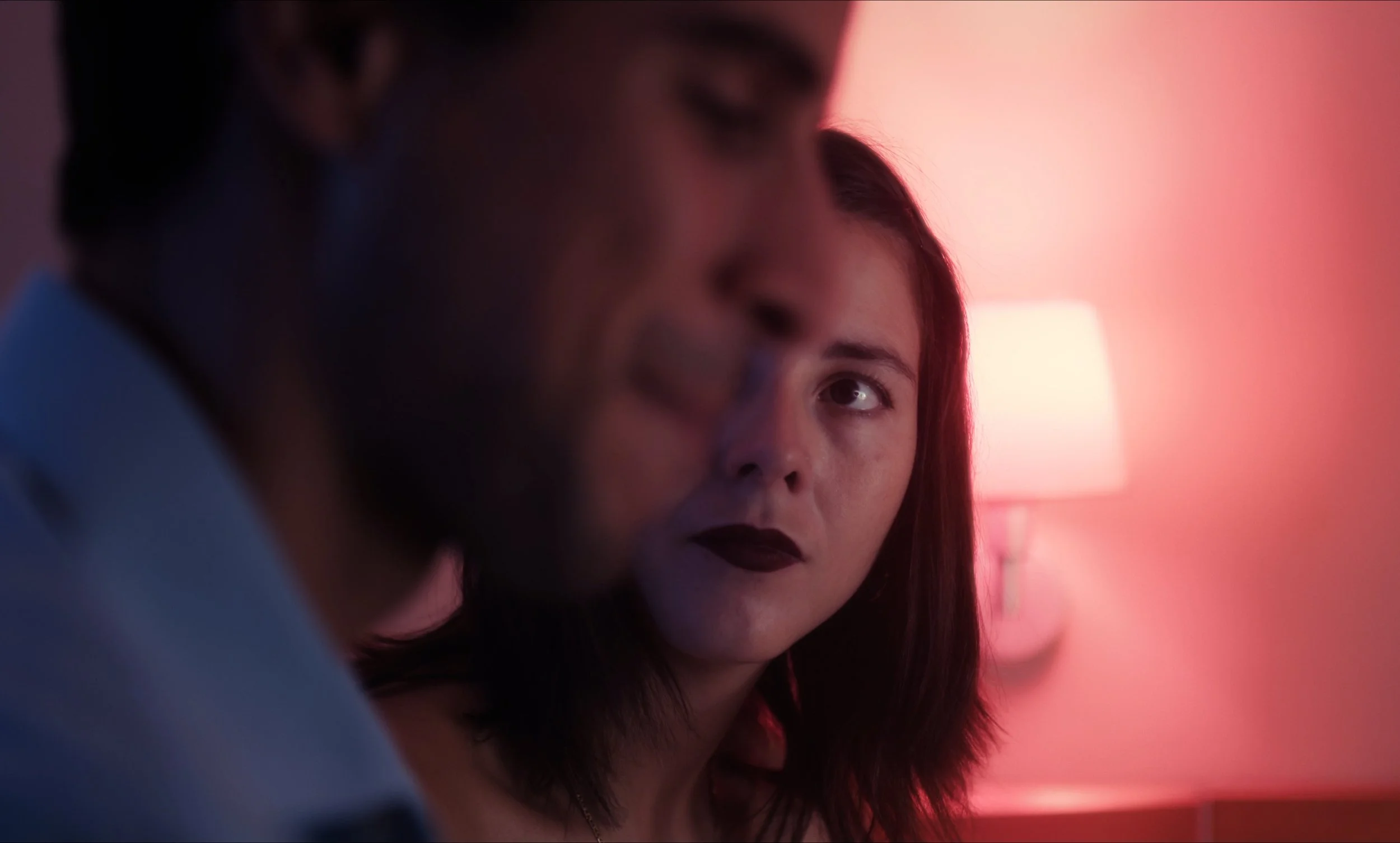 Una mujer mirando a un hombre en primer plano, con iluminación roja en el fondo.