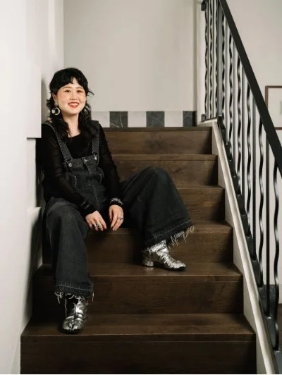 Person sitting on wooden stairs wearing black overalls and metallic silver boots.