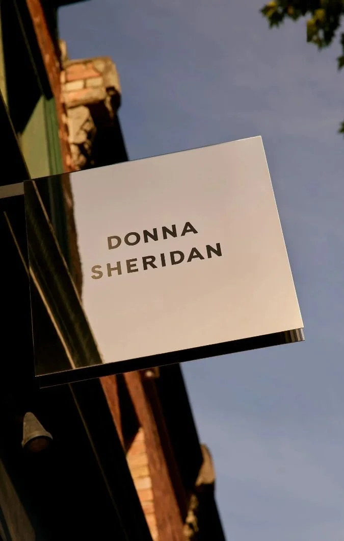 Hanging storefront sign with the text 'Donna Sheridan' against a blue sky.