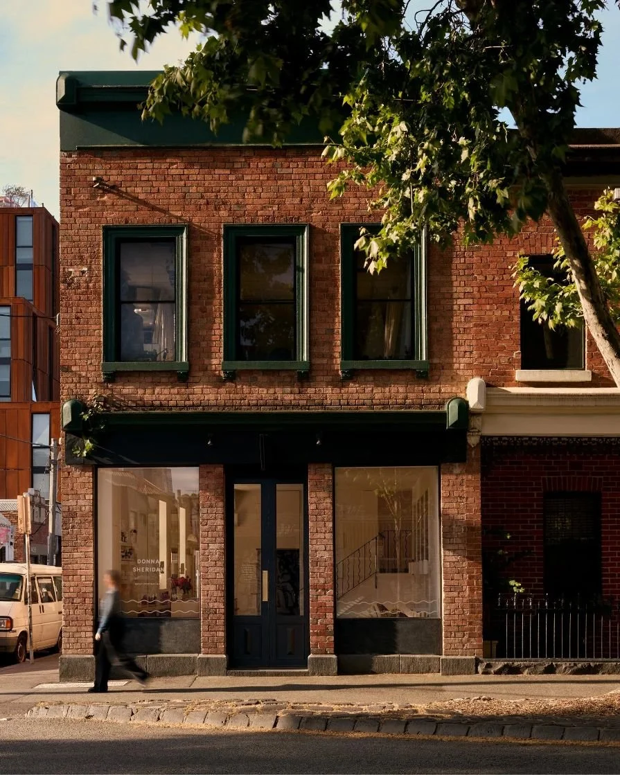 Exterior of Donna Sheridan Hair salon in Fitzroy, featuring a restored brick facade, large street-facing windows, and warm afternoon light beneath leafy trees.