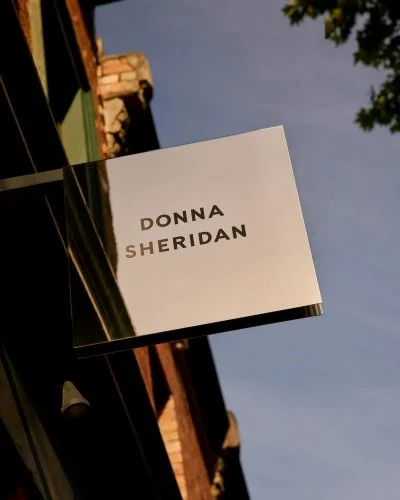 Minimal Donna Sheridan Hair hanging sign photographed against a warm evening sky and heritage Fitzroy streetscape.