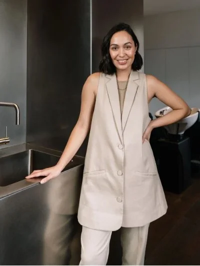 Person wearing a beige vest suit standing by a modern kitchen sink, smiling.