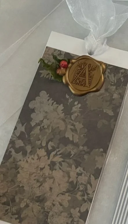 A decorative gift tag with a gold wax seal, red berries, and green sprigs on a floral-patterned envelope.