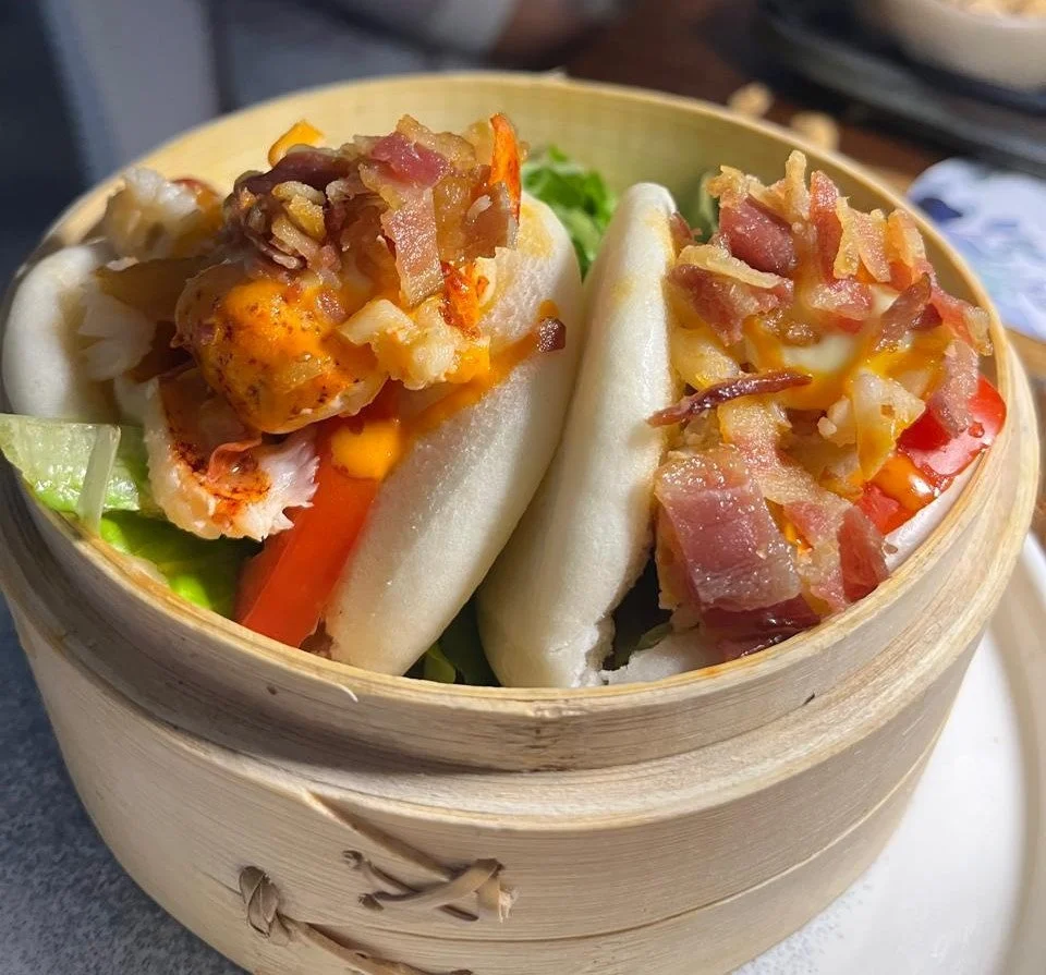 Dim sum basket filled with bao buns topped with bacon, cheese, and vegetables.