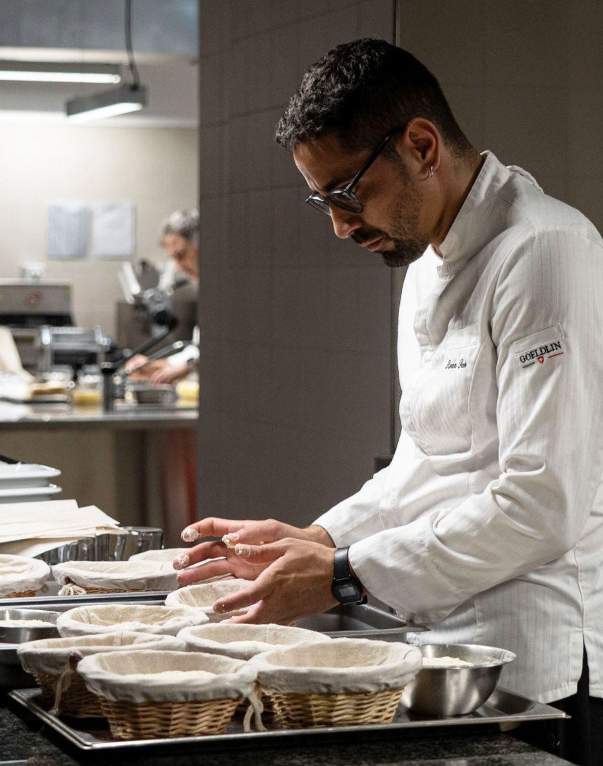 A chef in a white uniform preparing bread in a professional kitchen.