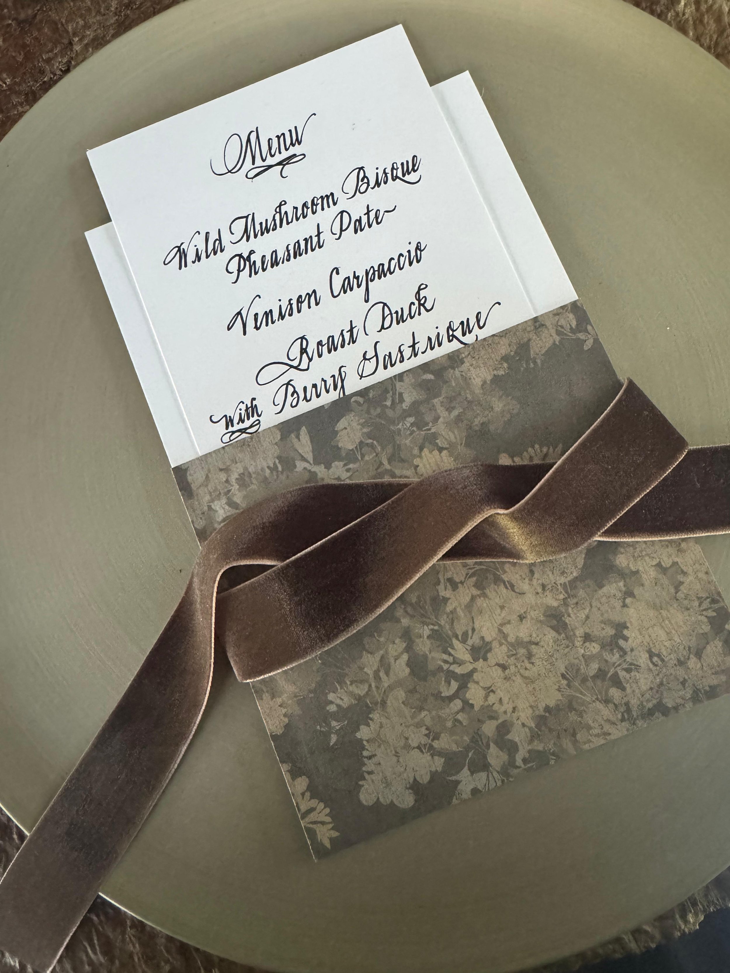 A menu on a piece of paper with black cursive text listing various food items, placed on a textured surface with a decorative ribbon.