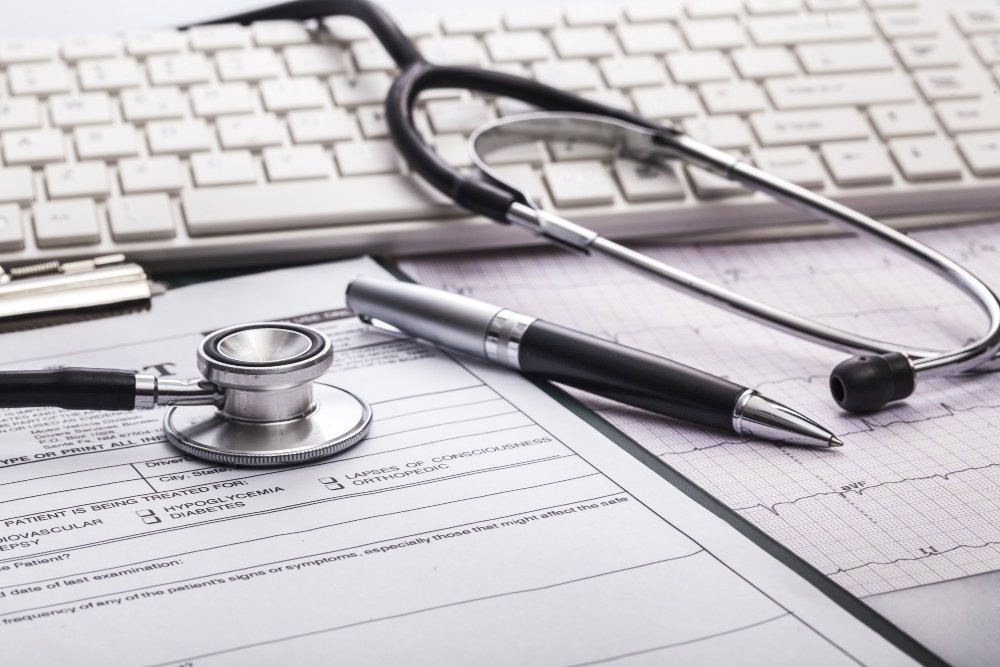 A stethoscope, a pen, and an electrocardiogram (ECG) printout on a desk with a keyboard in the background.
