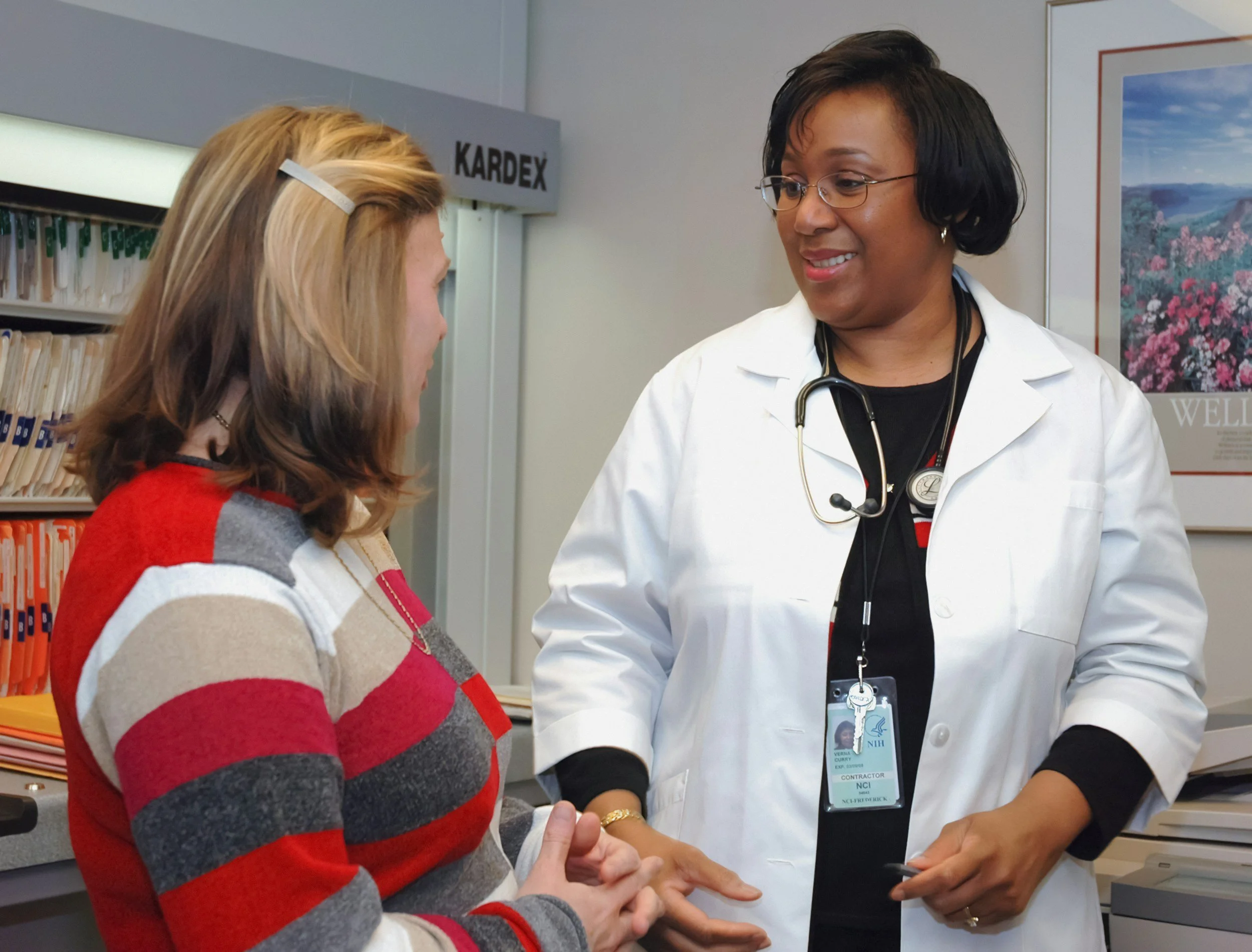 A medical professional is comforting a patient in a hospital room, with a female nurse and a skeleton model in the background.