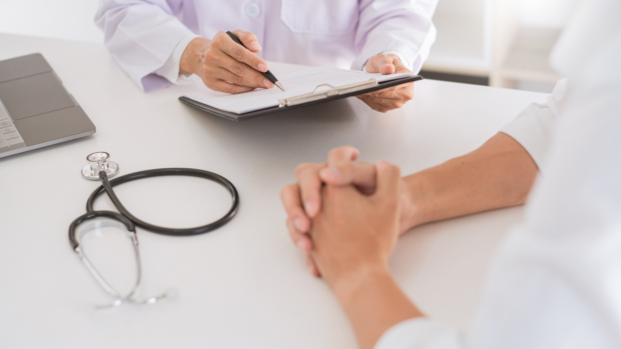 Doctor and patient holding hands during a consultation with a stethoscope and laptop on the table