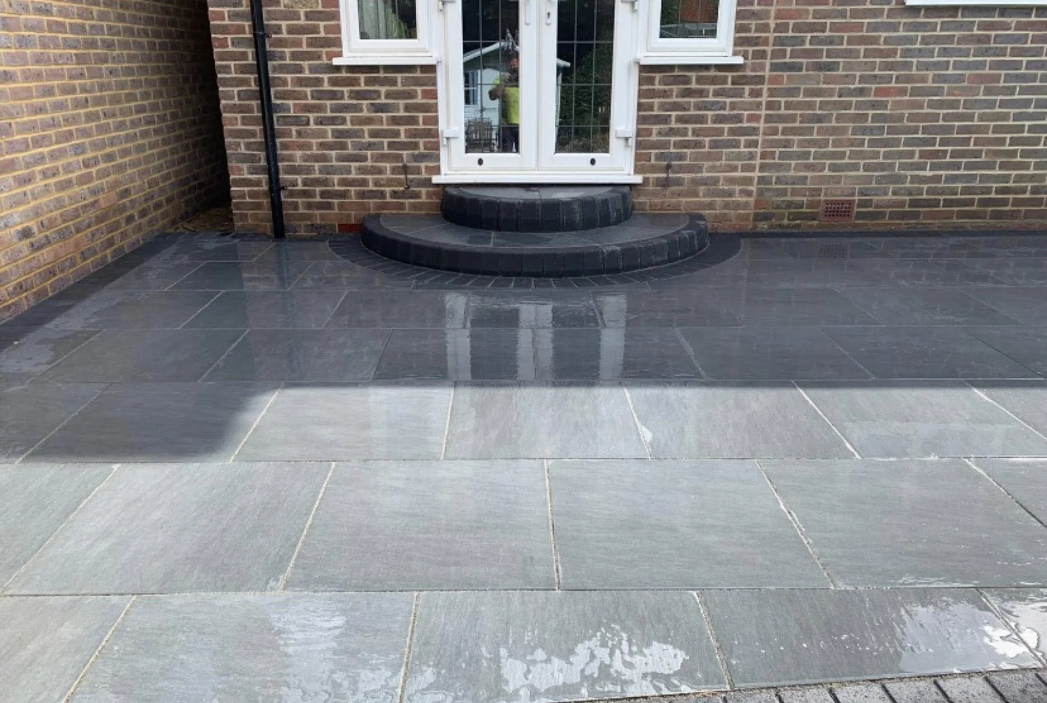 Clean gray stone patio with black circular steps leading up to glass patio doors on a brick house exterior.