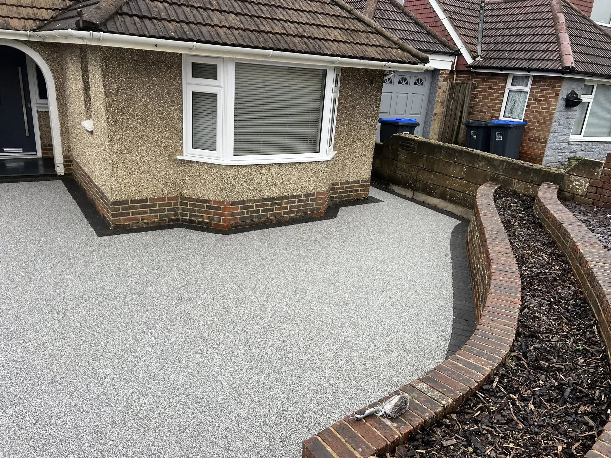 Freshly laid gravel in front yard of a house, with a curved brick flower bed border, and a small hedgehog near the edge of the bed.