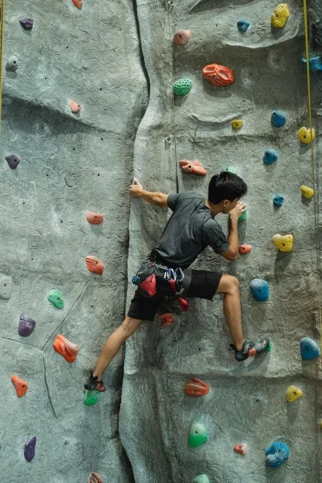 A boy rock climbing indoors with ropes.