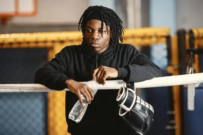 A boy with a discerning look on his face, holding boxing gloves and water.