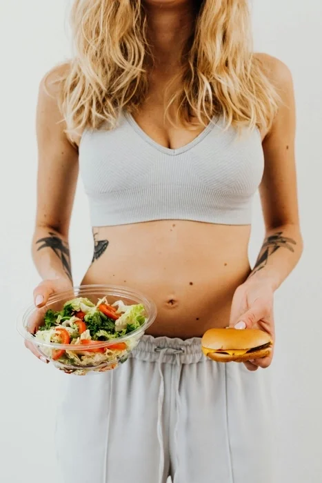 A woman holding a burger in one hand and a salad in another.