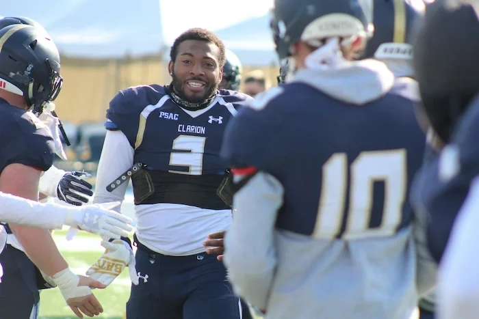 A football player surrounded by his team with his helmet off. He is smiling.