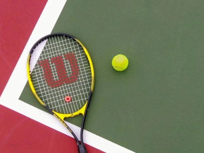 A yellow tennis racquet laying on the court next to a tennis ball.