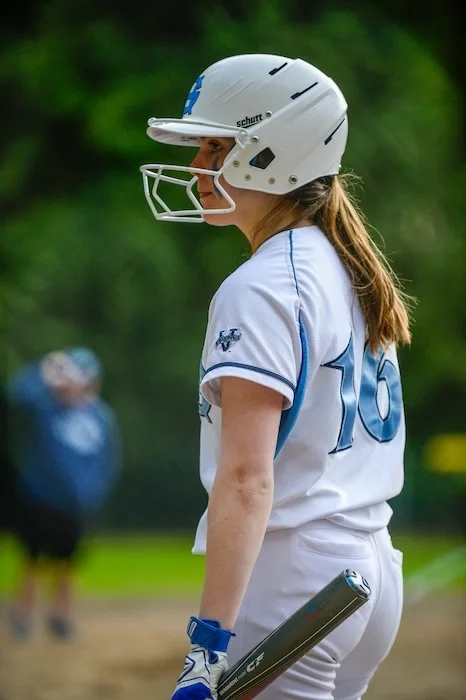 Softball player with a bat in her hand, looking off to the side.