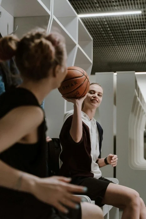 Teen girls talking with a basketball in a lockeroom.