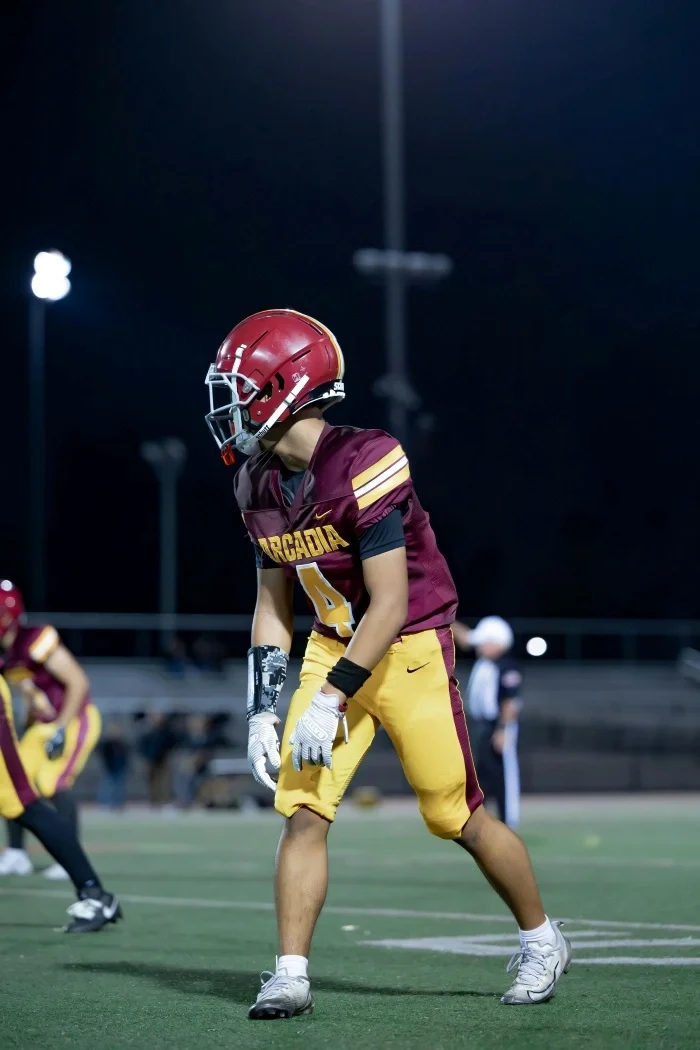 A high school football player in red and yellow team colors at night.