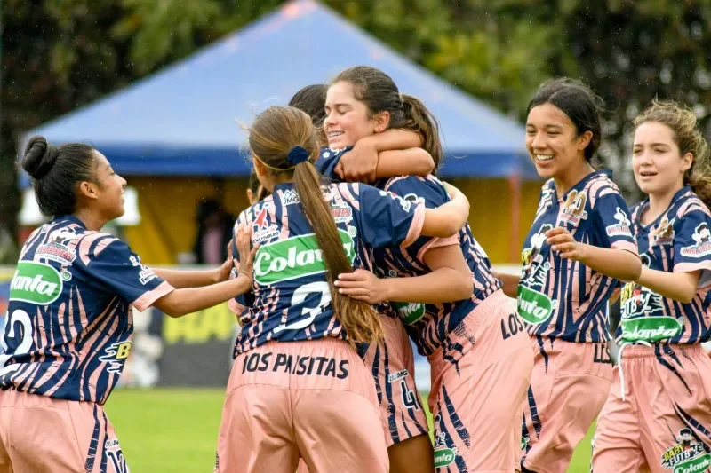 A teen girls' sports team smiling and celebrating on the field.