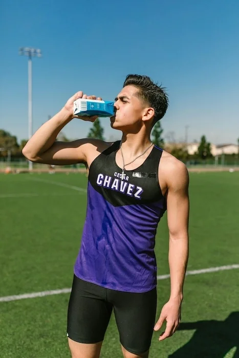 Teen athlete drinking from a small carton on a soccer field.