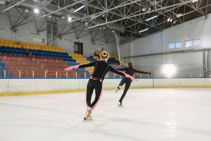 Two girls ice skating indoors.