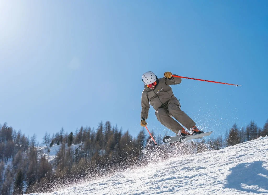 image of skier doing jump with blue sky, trees and mountains in background