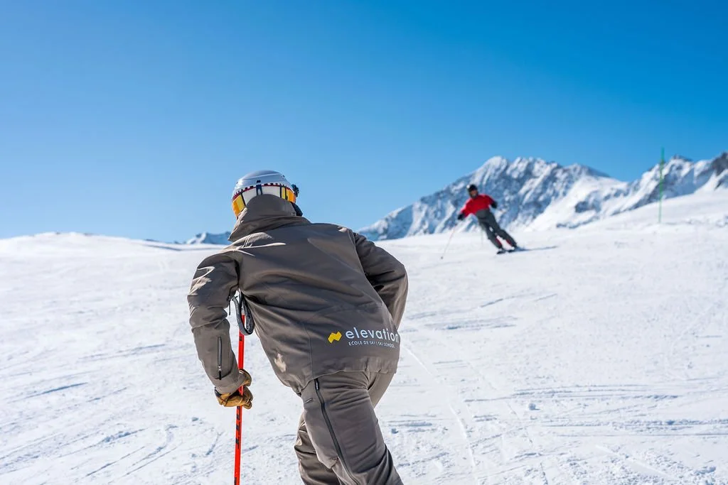 image shows Elevation ski instructor Nicko Braxton giving lesson with skier, mountains and blue sky in background