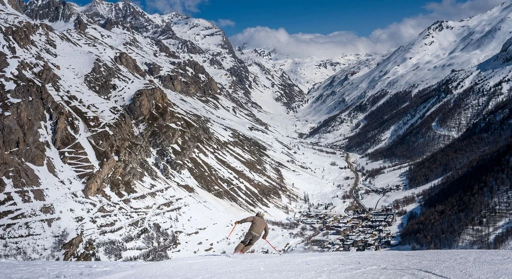 image of skier with Val d'Isère, mountains, snow, and blue sky in the background